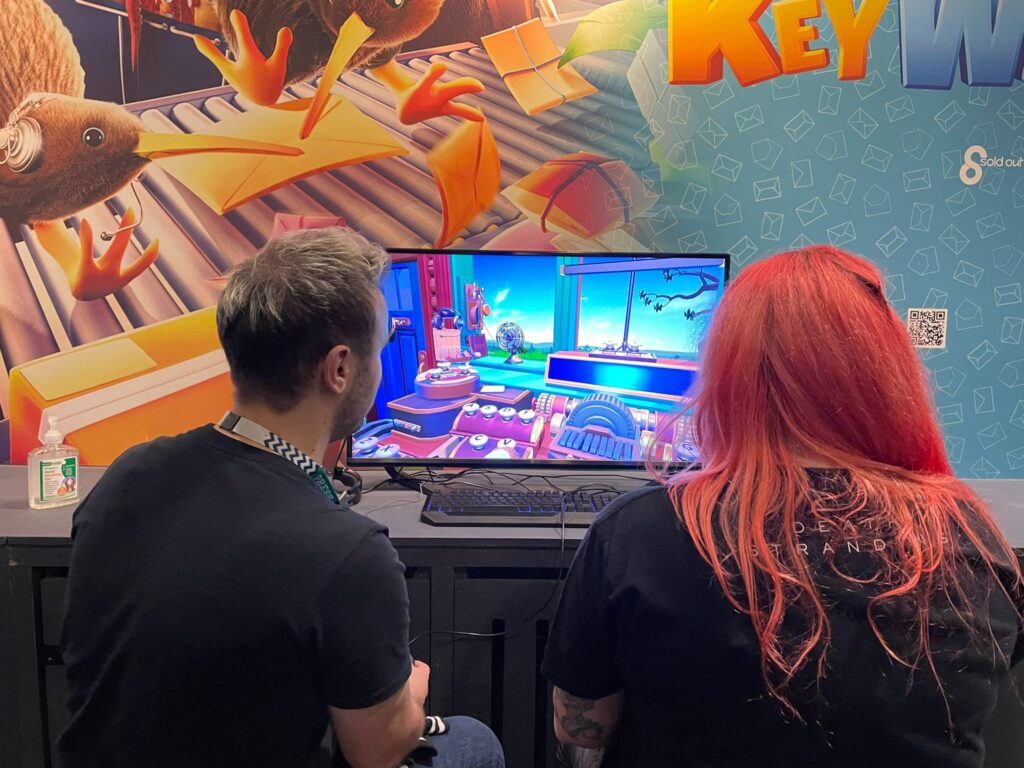 Two people sit at the same screen playing KeyWe together at its EGX booth.