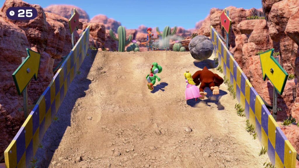 Yoshi, Peach and Donkey Kong climb up a steep desert hill as Mario throws boulders towards them.