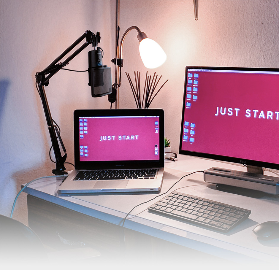 The microphone clipped to the side of a desk next to a laptop and monitor
