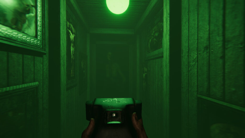 The main character holds a camera, looking down a green dimly lit hallway with a figure lurking at the end in the doorway.