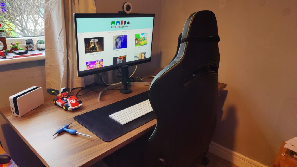 A monitor and mario kart sits on a large wooden desk in a seated height. The screen is showing the home page of Rapid Reviews UK.