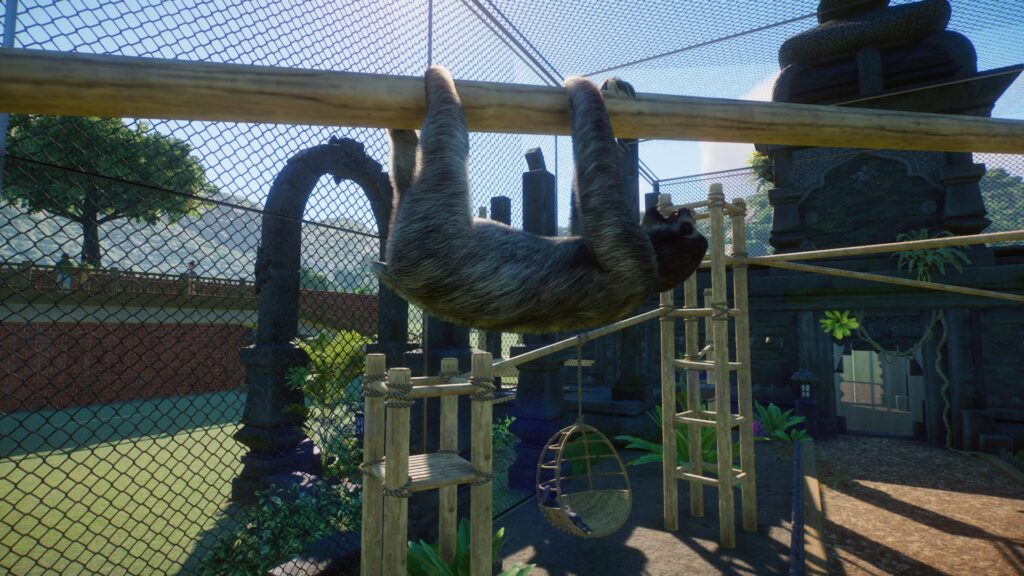 A sloth hangs from a beam in an enclosure.