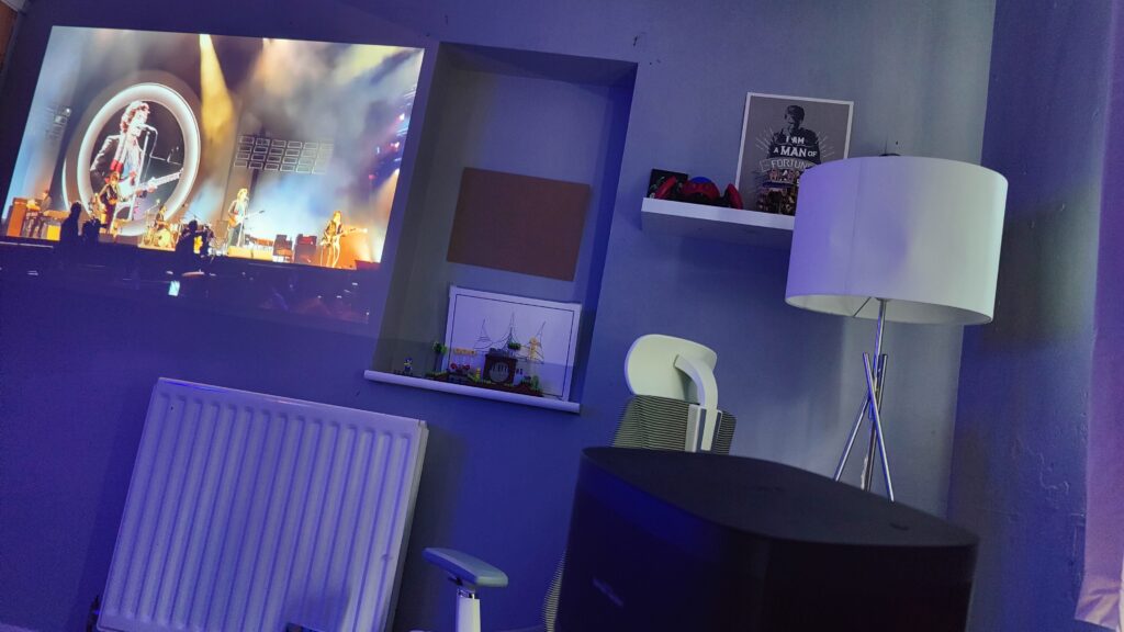 A projector at a 30 degree angle is projecting vide of Arctic Monkeys in a modern home office environment