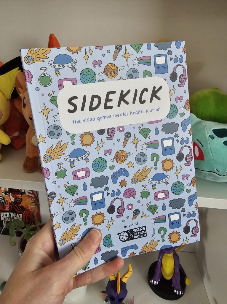 The Sidekick journal being held up against a bookshelf with plushies on