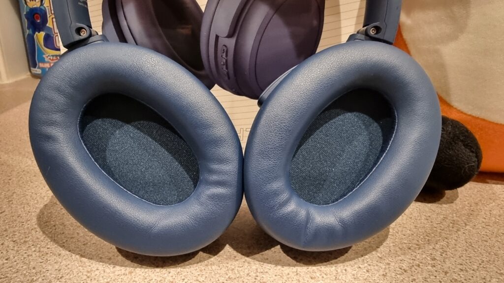 A close-up photograph of the ear cups of the Edifier WH700NB wireless headphones in navy blue; soft leather cups with fabric covering the speakers.